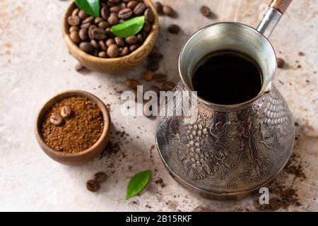 Morgenkaffeekonzept. Türkischer Kaffee in Turk und Kaffeebohnen auf einem Stein- oder Schieferkontertop. Stockfoto