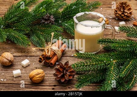 Weihnachts-Eggnog-Likör oder Cola de Mono-Cocktail. Klassisches Wintergetränk im Glasbecher, Weihnachtsdekoration. Immergrüne Äste, Zimt, Walnüsse, Zucker Stockfoto
