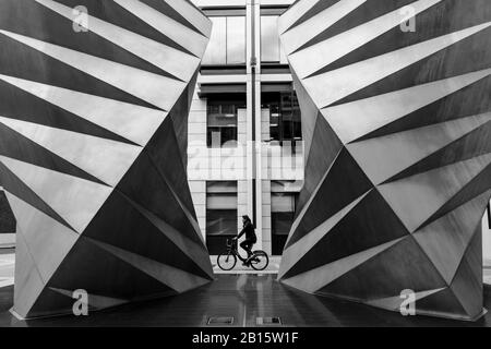 Londoner Schwarz-Weiß-Stadtfotografie: Radfahrer passiert Paternoster-Schlitze, eine Edelstahlskulptur von Thomas Heatherwick. City of London, Großbritannien Stockfoto