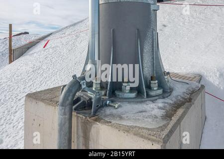 In den schneebedeckten Bergen ist eine Stahlsäule mit riesigen Schrauben an einem Betonfundament befestigt Stockfoto