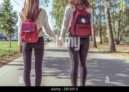 Zwei Mädchen Freundinnen im Sommer in der Stadt, die sich gegenseitig die Hände halten, Blick von hinten, Herbsttag, Rückkehr von Schule und Institut, Rucksäcke dahinter Stockfoto