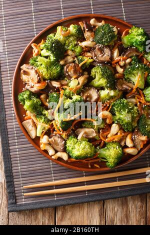 Vegetarisch rühren Sie in einem Teller auf dem Tisch schmorige Shiitake-Pilze, Brokkoli, Karotten und Cashewnüsse. Vertikale Draufsicht von oben Stockfoto