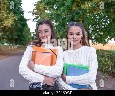 Zwei Freundinnen Mädchen Schulmädchen, im Sommer im Park, fröhliches Lächeln freuen sich, in Ordnern Mappen Notizbücher und Notizen mit Lehrbüchern. Ruhen Sie sich auf einer Pause aus Stockfoto