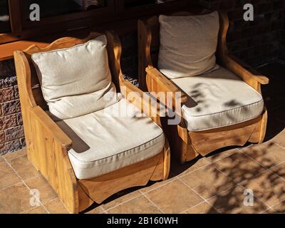 Zwei Holzstühle mit weichen Stoffsydles stehen auf gefliestem Boden, der von der Sonne beleuchtet wird Stockfoto