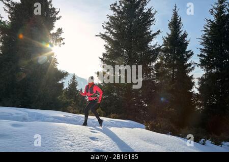 Der Trailrunner in pinkfarbener Jacke, Frau, die im Winter in den Bergen unterwegs ist, ist auf Schnee. Stockfoto