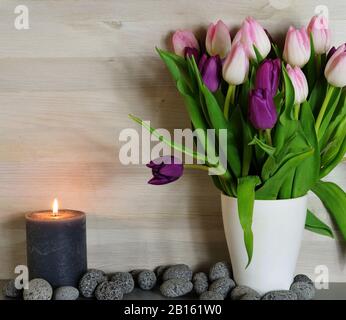 Ein Haufen rosafarbener und violetter Tulpen neben einer brennenden Kerze Stockfoto