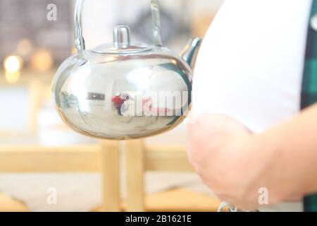 Schwangere junge Frau hält einen Wasserkocher Stockfoto