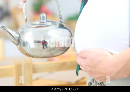 Schwangere junge Frau hält einen Wasserkocher Stockfoto