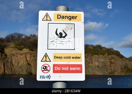 Warnschild Prestonhill Steinbruch Inverkeithing, bei dem es zu Todesfällen gekommen ist. Tiefes kaltes Wasser, Gefahr des Ertrinkens, nicht schwimmen. Verschwommenes Wasser, Klippen. Stockfoto