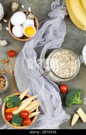 Lebensmittel: Tomateneier Walnüsse Bohnen Maisbrokkoli Karotten Bananen Haferbrei auf dunklem Hintergrund, natürliche Lebensmittel Draufsicht Flat Lay Stockfoto