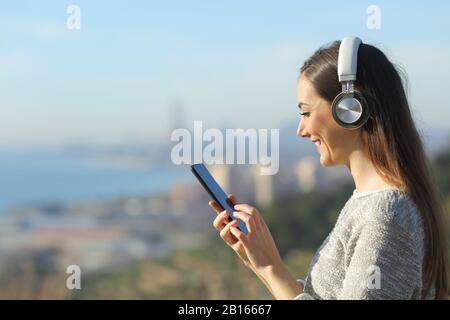 Glückliches Mädchen, das Smartphone verwendet, während er Musik mit Kopfhörern hört Stockfoto