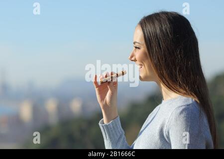 Fröhliches Mädchen, das eine Imbissbar am Stadtrand isst und dabei die Aussicht betrachtet Stockfoto