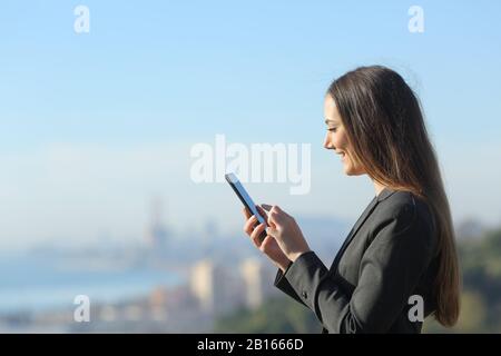 Seitenansicht eines glücklichen Geschäftsführers mit Smartphone in den Außenbezirken der Stadt Stockfoto