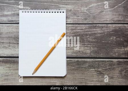 Notepad mit einem leeren weißen Blatt in einem Schachpapier mit einfachem Graphitstift liegt auf dem Hintergrund von Holzbrettern Stockfoto