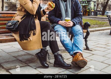 Bild beschneiden. Paar sitzt auf der bank Essen fast food Tee trinken. Stockfoto