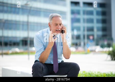Irritierter Geschäftsmann, der über das Handy spricht Stockfoto