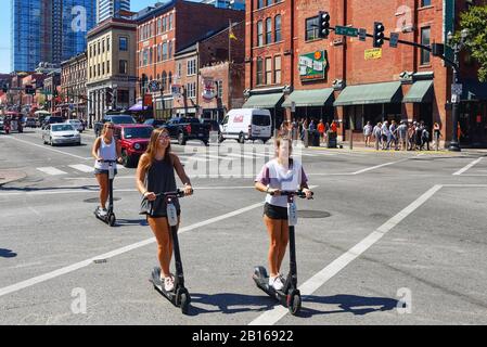 Nashville, TN, USA - 21. September 2019: Junge Frauen fahren Roller auf der Broadway Street. Die gemeinsame Nutzung von Rollern ist in der Stadt beliebt. Stockfoto
