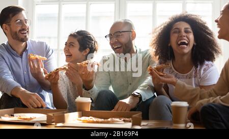 Lachen Sie mehrere Rassenfreunde, die im Haus Pizza essen Stockfoto