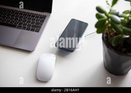 Overhead-Ansicht der Computermaus mit Laptop und Handy auf dem drahtlosen Ladegerät Stockfoto