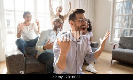 Aufgeregte multikulturelle Freunde, die im tv-Sportspiel zusehen, fühlen sich euphorisch Stockfoto