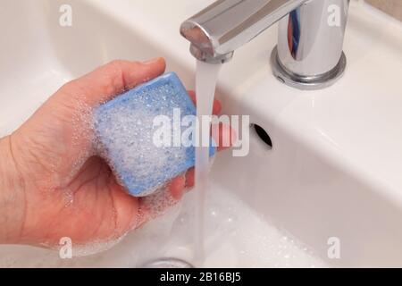 Halten Sie eine blaue Seifenleiste unter fließendem Wasser in einem Waschbecken. Medizinisches Reinheitskonzept Stockfoto