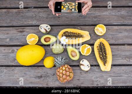 Photographing on smart phone variety of exotic fruits and berries on the wooden table Stockfoto