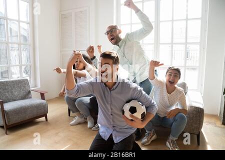 Aufgeregte multiethnische Freunde feierten den Fußballsieg im Innenbereich Stockfoto