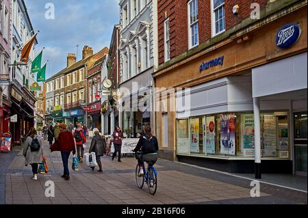 Straßenszene im Stadtzentrum von Norwich mit Menschen, die an Geschäften und Büros vorbeilaufen und mit dem Fahrrad fahren Stockfoto