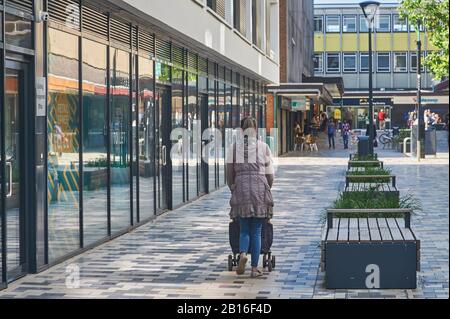 Eine Dame, die einen Liegestuhl an den Bürogebäuden mit Glasfront im Zentrum von Stevenage, Hertfordshire vorbeitreibt Stockfoto