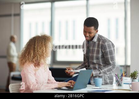 Portrait des jungen afroamerikanischen Mannes, der ein Geschäftsprojekt mit einer weiblichen Kollegin im modernen Büro diskutiert, Copy-Space Stockfoto