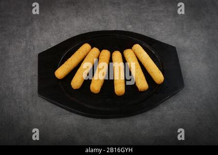 Gebratene Mozzarella klebt knusprig auf einer schwarzen Wollplatte, die auf dunkelgrauem Hintergrund isoliert ist Stockfoto