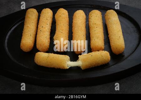 Gebratene Mozzarella klebt knusprig auf einer schwarzen Wollplatte, die auf dunkelgrauem Hintergrund isoliert ist Stockfoto