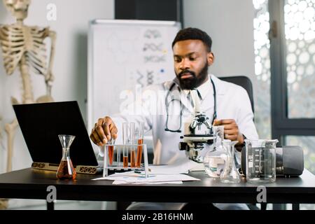 Forscher des Afrikanischen Wissenschaftlers, der im Labor am Tisch sitzt und DNA-Tests, Analisys von Blutproben oder neuen Substanzen macht, untersuchen Testwanne Stockfoto