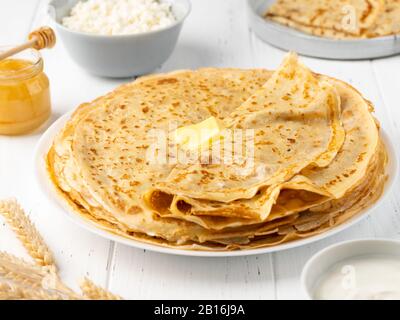 Crepes mit Butter, Honig, Sauerrahm, Hüttenkäse und Weizenkorn auf weißem Holzhintergrund. Hausgemachtes gesundes Frühstück. Stockfoto