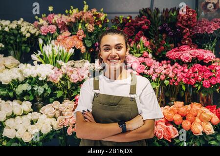 Frau Floristin steht im Blumenladen. Weibliche Floristin in Schürze, die mit gekreuzten Armen steht. Stockfoto