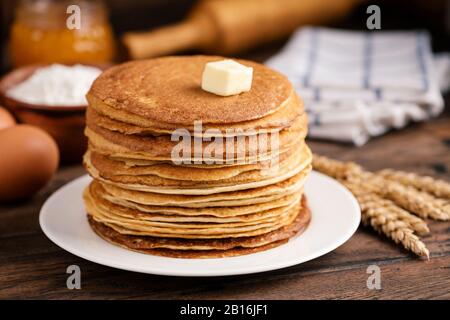 Ein Stapel mit Blini, russischen dünnen Pfannkuchen oder Crepes mit Butter auf dem alten rustikalen Holztisch. Maslenitsa, Shrove Tuesday Concept Stockfoto