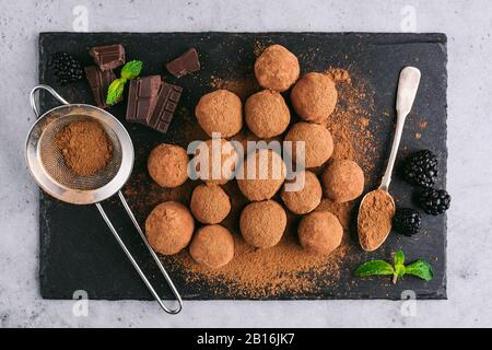 Schokoladentrüffel mit Kakaopulver und Minze auf schwarzem Schiefergrund, Draufsicht. Schmackhaftes süßes Schokoladenbonbon Stockfoto