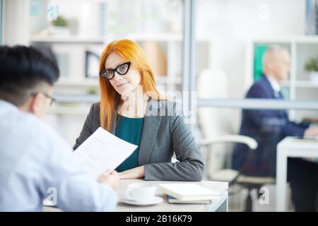 Porträt einer erwachsenen, rothaarigen Geschäftsfrau, die junge Männer zwecks Stellenbestellung im Büro interviewt, Kopierraum Stockfoto