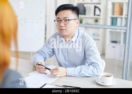 Portrait des jungen Asiaten, der während des Bewerbungsgesprächs Fragen beantwortet, gegenüber des HR-Managers, Copy-Space Stockfoto