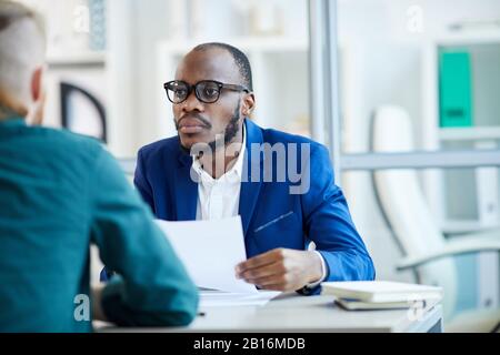Porträt eines zeitgenössischen afroamerikanischen Geschäftsmannes, der während eines Bewerbungsgesprächs im Büro dem Kandidaten zuhört, Kopie des Raums Stockfoto