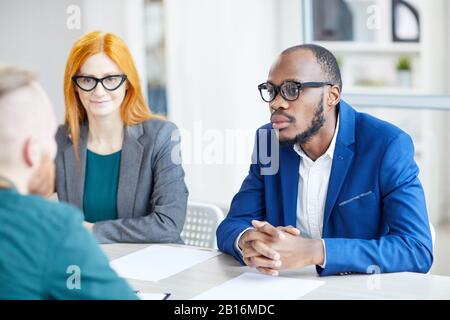 Porträt eines zeitgenössischen afroamerikanischen Geschäftsmannes, der während eines Bewerbungsgesprächs im Büro dem Kandidaten zuhört Stockfoto