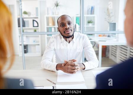 Porträt von zwei nicht erkennbaren Geschäftsleuten, die afroamerikanischen Mann für eine Position im Büro beinterviewen, Copy-Space Stockfoto