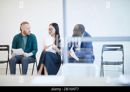 Multiethnische Gruppe von Menschen, die im Anschluss auf ein Bewerbungsgespräch warten und hinter der Glaswand plaudern, Kopierraum Stockfoto