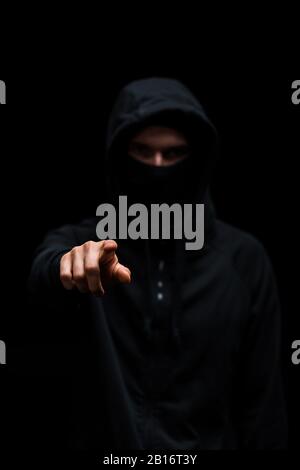 Selektiver Fokus des Hackers in der Kapuze, der mit einem auf Schwarz isolierten Finger zeigt Stockfoto