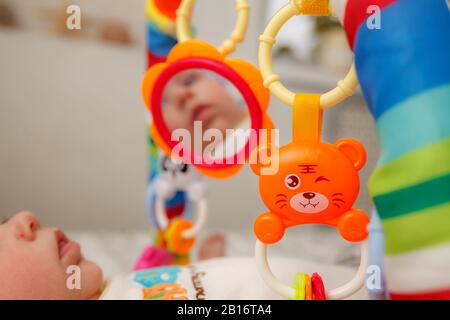 Baby sieht seine Reflexion in Spielzeug Spiegel auf Spielmatte. Spielzeug für Neugeborene und Anfänger zu kriechen Stockfoto