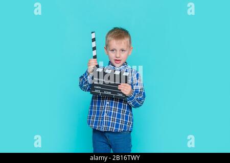 Lächelndes Kind, das Filmklapper auf blauem Hintergrund hält Stockfoto