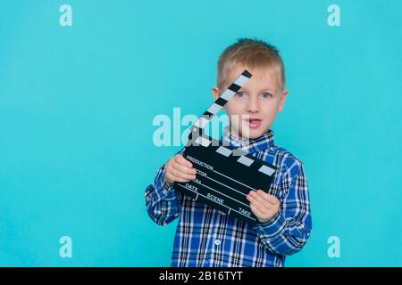 Lächelndes Kind, das Filmklapper auf blauem Hintergrund hält Stockfoto