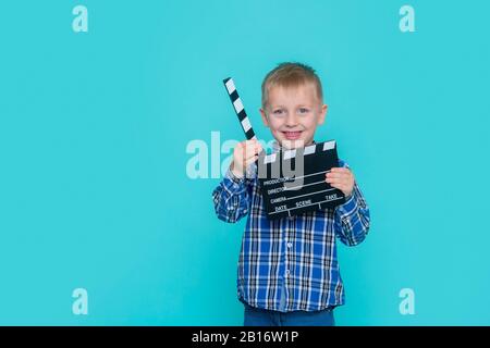 Lächelndes Kind, das Filmklapper auf blauem Hintergrund hält Stockfoto