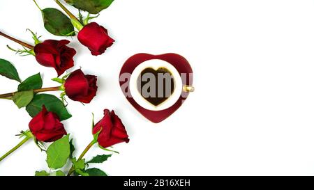 Rote Rosen kreative Komposition flaches Lay-Layout mit Kaffee in herzförmiger Tasse und Untertasse auf weißem Hintergrund, mit negativem Kopierraum. Stockfoto