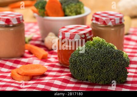 Nahaufnahme von frischen Brokkoli, Karotte und Blumenkohl mit Gläsern Babynahrung auf Tischdecke auf Holzoberfläche Stockfoto